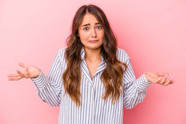 Pembe arka planda izole edilmiş genç beyaz kadın sorgulama sırasında omuz silkiyor ve şüphe duyuyor..