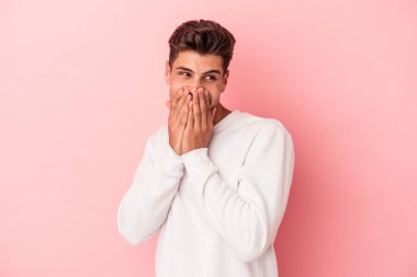 Pembe arka planda izole edilmiş genç beyaz bir adam bir şeye gülüyor, elleriyle ağzını kapatıyor..