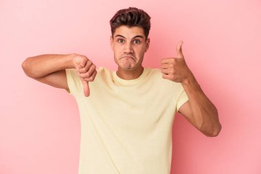 Pembe arka planda izole edilmiş genç beyaz bir adam baş parmağını kaldırıyor ve baş parmağıyla işaret ediyor. Zor bir seçim.