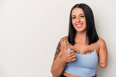 Beyaz arka planda tek kollu beyaz bir kadın gülümsüyor ve başparmağını kaldırıyor.