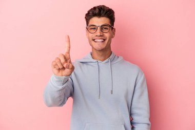 Pembe arka planda izole edilmiş genç beyaz bir adam bir numarayı parmağıyla gösteriyor..