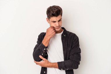 Beyaz arka planda izole edilmiş genç beyaz bir adam şüpheli ve şüpheci bir ifadeyle yana bakıyor..