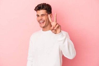 Pembe arka planda izole edilmiş genç beyaz adam iki numarayı parmaklarıyla gösteriyor..