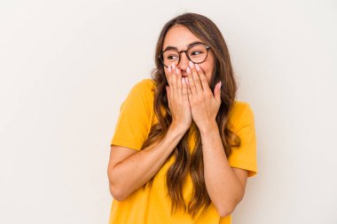 Beyaz arka planda izole edilmiş genç beyaz bir kadın bir şeye gülüyor, elleriyle ağzını kapatıyor..