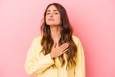 Pembe arka planda izole edilmiş genç beyaz kadın yemin ediyor, elini göğsüne koyuyor..