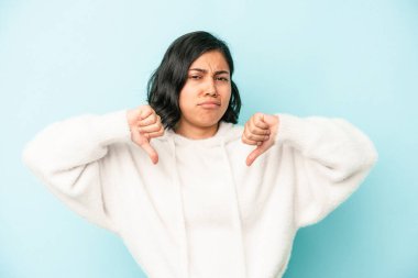 Mavi arka planda izole edilmiş genç Latin kadın baş parmağını aşağı gösteriyor, hayal kırıklığı konsepti..