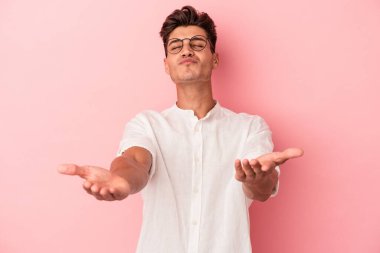 Genç beyaz adam pembe arka planda izole edilmiş dudaklar kıvrılmış ve hava öpücüğü göndermek için avuç içleri tutulmuş..