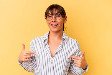 Arjantinli genç bir kadın, sarı arka planda izole edilmiş, parmakları aşağıda, olumlu hisler içinde..