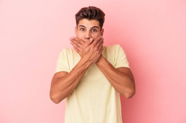 Pembe arka planda izole edilmiş genç beyaz adam elleriyle ağzını kapatırken şok oldu..