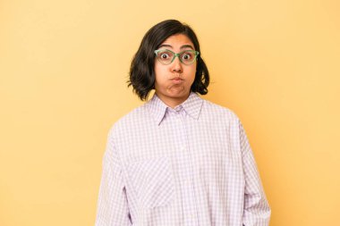 Sarı arka planda izole edilmiş genç Latin kadın yanakları patlatıyor, yorgun bir ifadesi var. Yüz ifadesi kavramı.