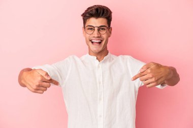 Pembe arka planda izole edilmiş genç beyaz adam parmaklarıyla aşağıya doğru, olumlu bir his..