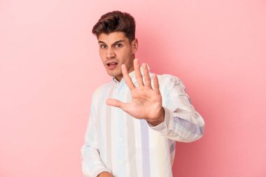 Pembe arka planda izole genç beyaz adam yakın bir tehlike nedeniyle şoka uğruyor.