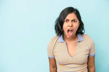 Mavi arka planda izole edilmiş genç Latin bir kadın çok kızgın, öfkeli, hayal kırıklığına uğramış.