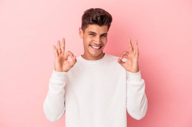 Pembe arka planda izole edilmiş genç beyaz adam neşeli ve kendinden emin, iyi bir hareket gösteriyor..