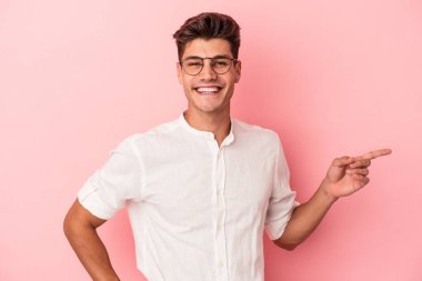 Pembe arka planda izole edilmiş genç beyaz adam işaret parmağıyla işaret ederek gülümsüyor..