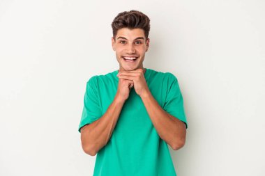 Beyaz arka planda izole edilmiş genç beyaz bir adam şans için dua ediyor, şaşırmış ve ağzını açıp önüne bakıyor..