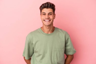 Pembe arka planda izole edilmiş genç beyaz adam mutlu, güler yüzlü ve neşeli.