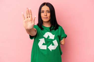 Bir kolu geri dönüşümlü, pembe arka planda izole edilmiş, elini uzatmış, dur işareti gösteren beyaz bir kadın..