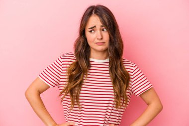 Pembe arka planda izole edilmiş genç beyaz kadın kafası karışmış, kuşkulu ve güvensiz hissediyor..