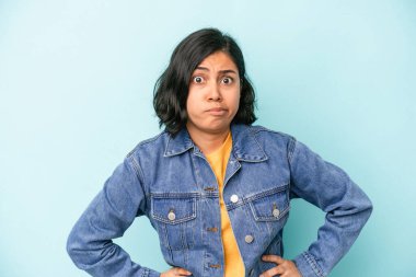 Mavi arka planda soyutlanmış genç Latin kadın kafası karışmış, kuşkulu ve güvensiz hissediyor..