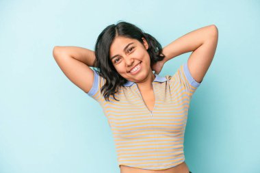 Mavi arka planda izole edilmiş genç Latin bir kadın. Kollarını uzatıyor, rahat bir konumda..