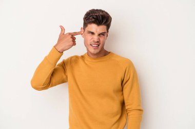 Beyaz arka planda izole edilmiş genç beyaz bir adam kulaklarını elleriyle kapatıyor..