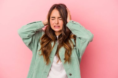 Pembe arka planda izole edilmiş genç beyaz kadın kulaklarını elleriyle kapatıyor..