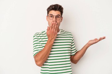 Beyaz arka planda izole edilmiş genç beyaz adam, avuç içi fotokopi alanını elinde tutmaktan etkilenmiş..