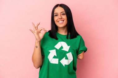 Tek kolu geri dönüşümlü, pembe arka planda izole edilmiş, neşeli ve kendine güvenen beyaz bir kadın..