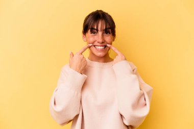 Arjantinli genç bir kadın sarı arka planda izole edilmiş gülümsüyor ve parmaklarını ağzına doğrultuyor..