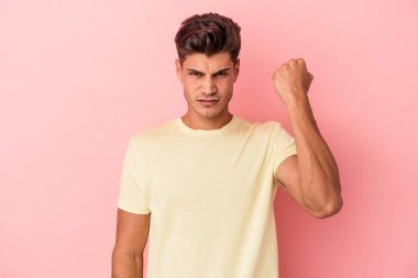 Pembe arka planda izole edilmiş genç beyaz adam yumruğunu kameraya gösteriyor, agresif yüz ifadesi var..