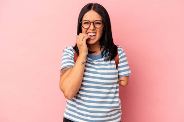 Tek kolu pembe arka planda izole edilmiş, tırnaklarını yiyen, gergin ve endişeli beyaz bir kadın öğrenci..