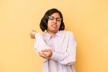 Genç Latin bir kadın sarı arka planda izole edilmiş, dirsek masajı yapıyor, kötü bir hareketin ardından acı çekiyor..