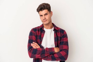 Beyaz arka planda izole edilmiş genç beyaz adam alaycı bir ifadeyle kameraya bakıyor..