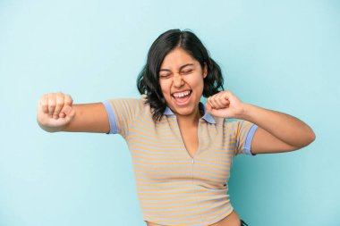 Mavi arka planda yalnız yaşayan genç Latin kadın dans ediyor ve eğleniyor..