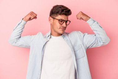 Pembe arka planda izole edilmiş genç beyaz bir adam güçlü bir hareket gösteriyor, kollarıyla, kadınsı gücün sembolü.