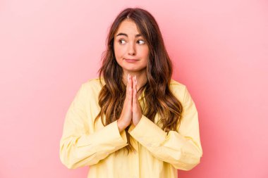 Pembe arka planda izole edilmiş genç beyaz kadın dua ediyor, bağlılık gösteriyor, dindar biri ilahi ilham arıyor..