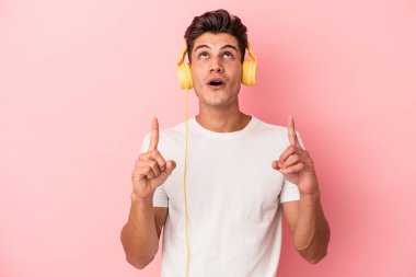 Pembe arka planda izole edilmiş müzik dinleyen beyaz bir adam ağzı açık bir şekilde üst tarafı işaret ediyor..