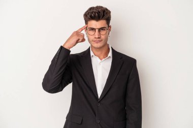Beyaz arka planda izole edilmiş kulaklık takan genç beyaz iş adamı şakağı işaret ediyor, düşünüyor ve bir göreve odaklanıyor..