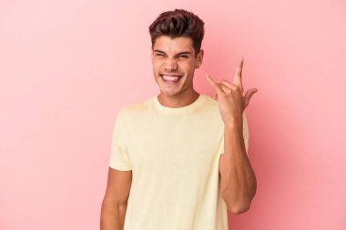 Pembe arka planda izole edilmiş genç beyaz adam parmaklarıyla taş hareketi gösteriyor.