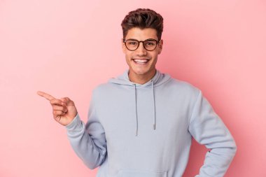 Pembe arka planda izole edilmiş genç beyaz adam işaret parmağıyla işaret ederek gülümsüyor..