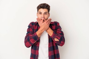 Beyaz arka planda izole edilmiş genç beyaz adam elleriyle ağzını kapatırken şok oldu..