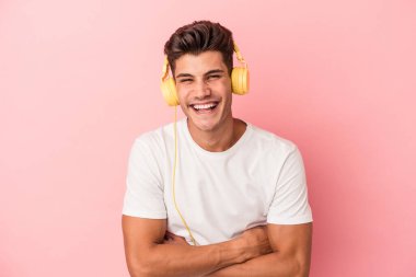 Pembe arka planda izole edilmiş müzik dinleyen beyaz bir adam gülüyor ve eğleniyor..