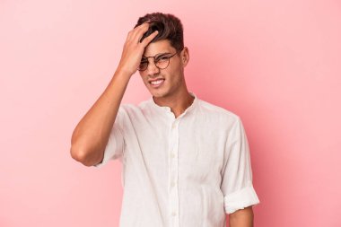 Pembe arka planda izole edilmiş genç beyaz bir adam bir şeyi unutuyor. Alnına avuç içi ve gözlerini kapatarak vuruyor..