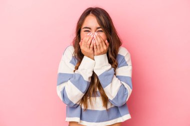 Pembe arka planda izole edilmiş genç beyaz kadın bir şeye gülüyor, elleriyle ağzını kapatıyor..