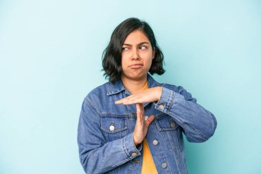 Mavi arka planda izole edilmiş genç Latin kadın bir mola hareketi gösteriyor..