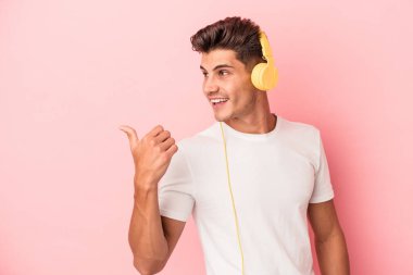 Pembe arka planda müzik dinleyen beyaz bir adam. Baş parmak uzakta, gülüyor ve kaygısız..