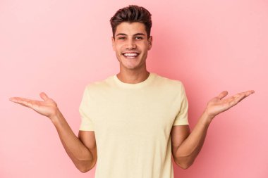 Pembe arka planda izole edilmiş genç beyaz adam kollarıyla ölçek oluşturuyor, mutlu ve kendinden emin hissediyor..