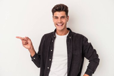 Beyaz arka planda izole edilmiş genç beyaz adam işaret parmağıyla işaret ederek gülümsüyor..