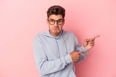 Pembe arka planda izole edilmiş genç beyaz adam işaret parmağıyla fotokopi alanını işaret ederek şok oldu..